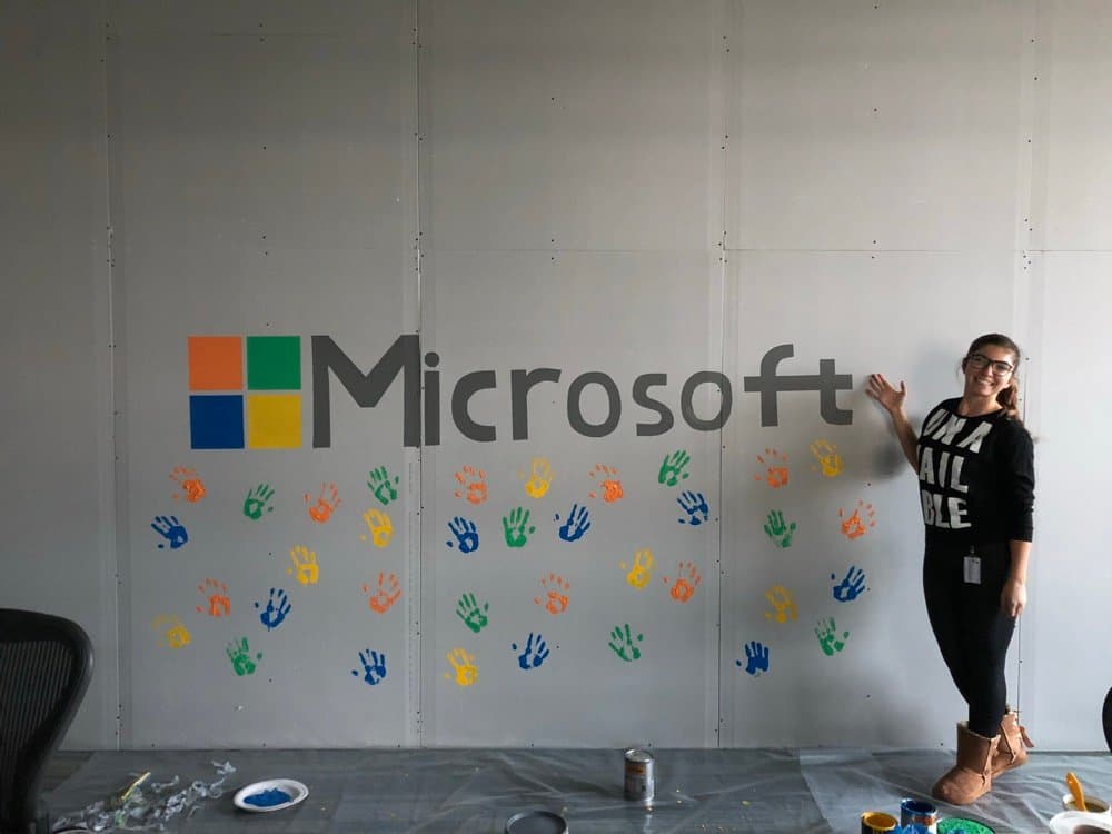 Ecem beside a Microsoft wall with painted handprints